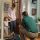 A Bath Fitter installer is kneeling at the front door with an excited child and happy mom greeting him from the front door of their house.