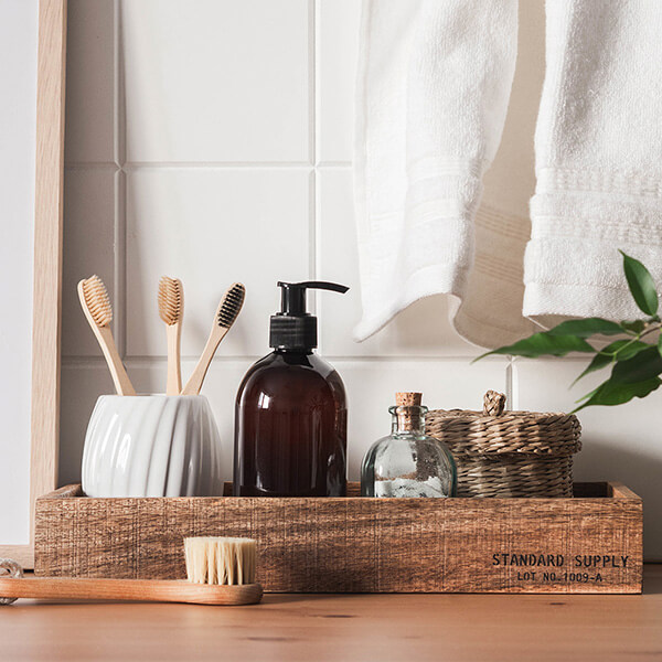 Bath accessories, cosmetic bottles and toothbrushes are displayed on a wooden bathroom shelf.