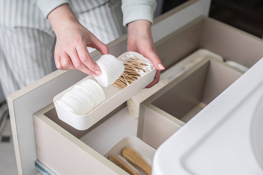 A female is organizing toiletries in an open bathroom vanity drawer, under the sink.