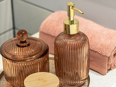 A glass copper soap dispenser is seated on a metallic tray on a bathroom sink